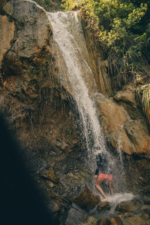 a man stands in a body of water near a waterfall