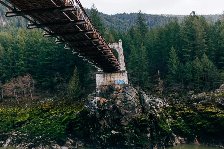 an empty, bridge sitting above a river in the mountains