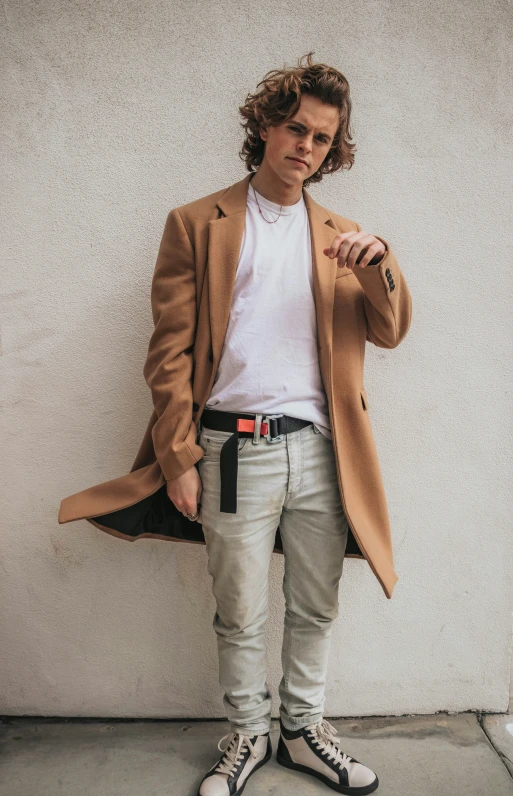 a man stands against a wall, posing in his outfit and a scarf