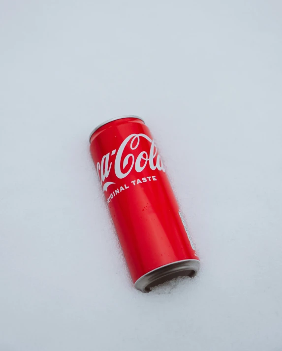 an open red can of coca - cola sitting on top of white snow
