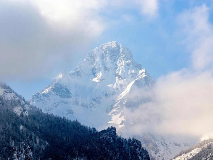 the mountains with clouds are covered in snow