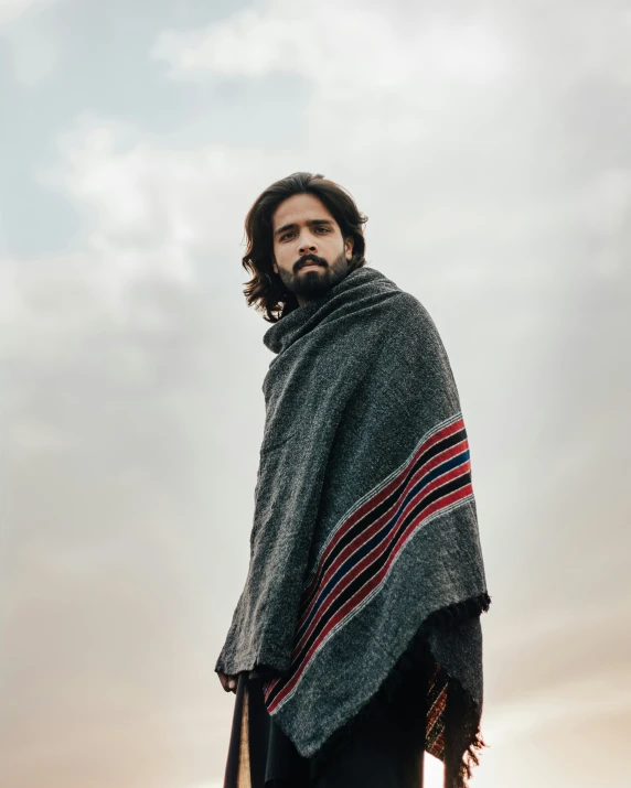 the man stands on a beach and is wrapped in a blanket