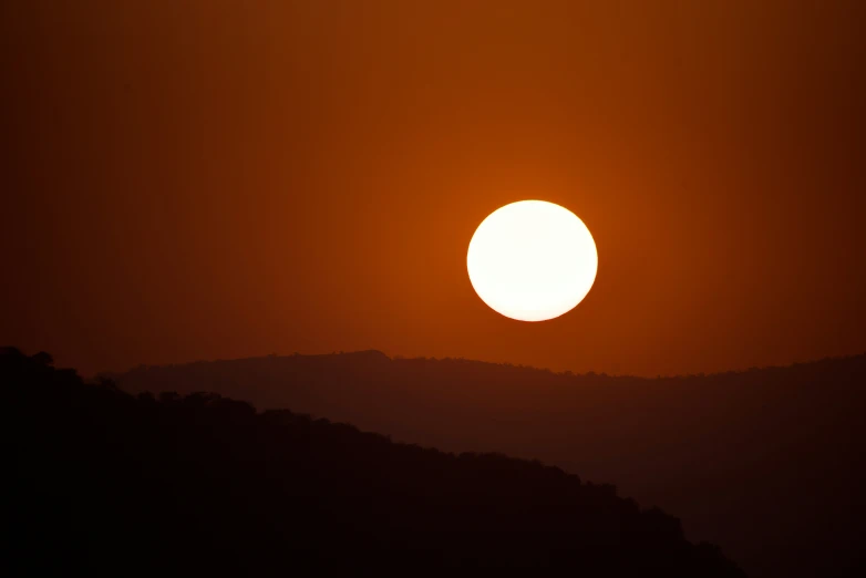 the sun is in the distance as it sets on a mountain