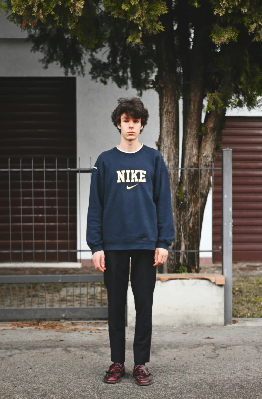 a young man standing on a street wearing nike sweatshirt