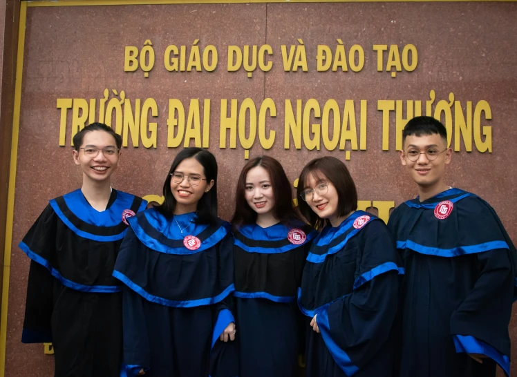 four graduates smile for the camera while posing in front of a brown wall