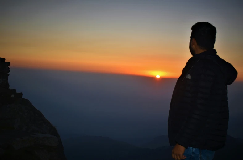 a man is looking out over a foggy mountain at sunrise