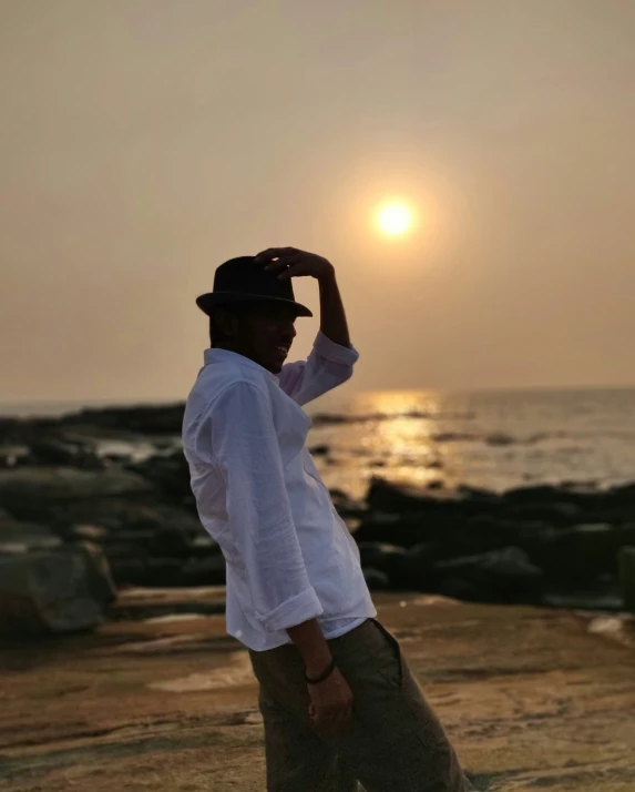 a man holding his hat as he looks over the ocean