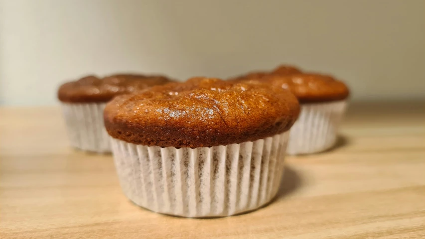 three muffins sitting in white paper cups on a counter