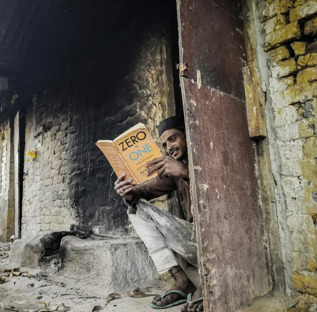 a man leaning against a building while holding an open book