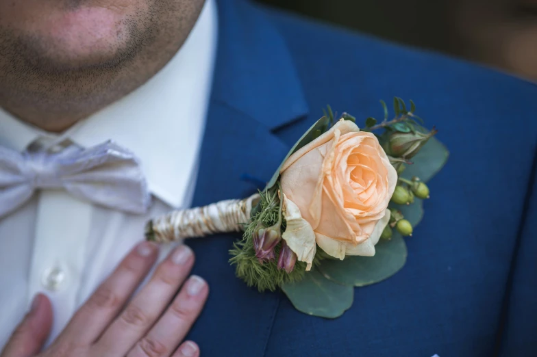 a groom in blue suit holding a peach colored rose