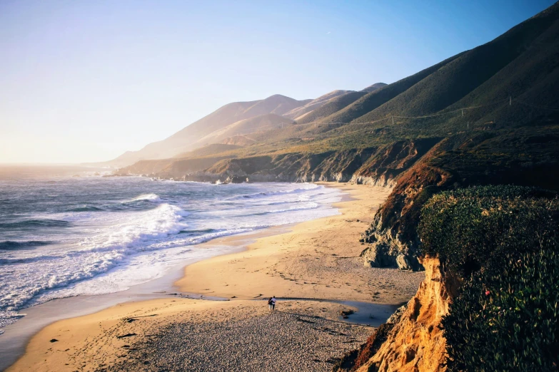 a beach with the ocean and hills in the background