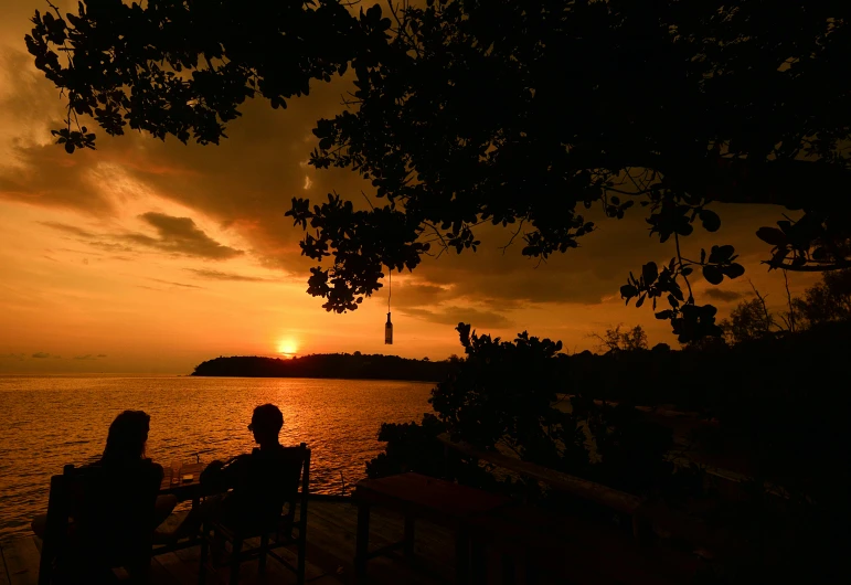 a sunset on the water with two people sitting