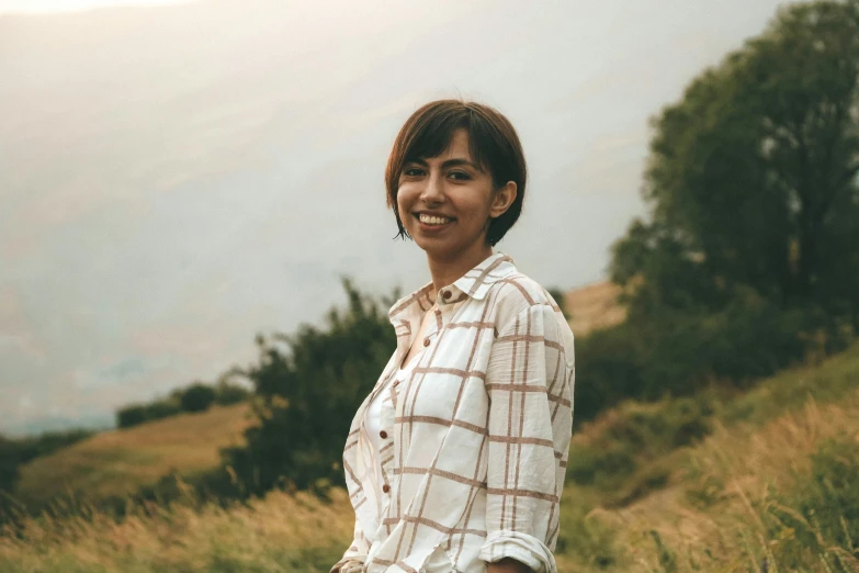 a woman standing on a grassy hill with trees in the background