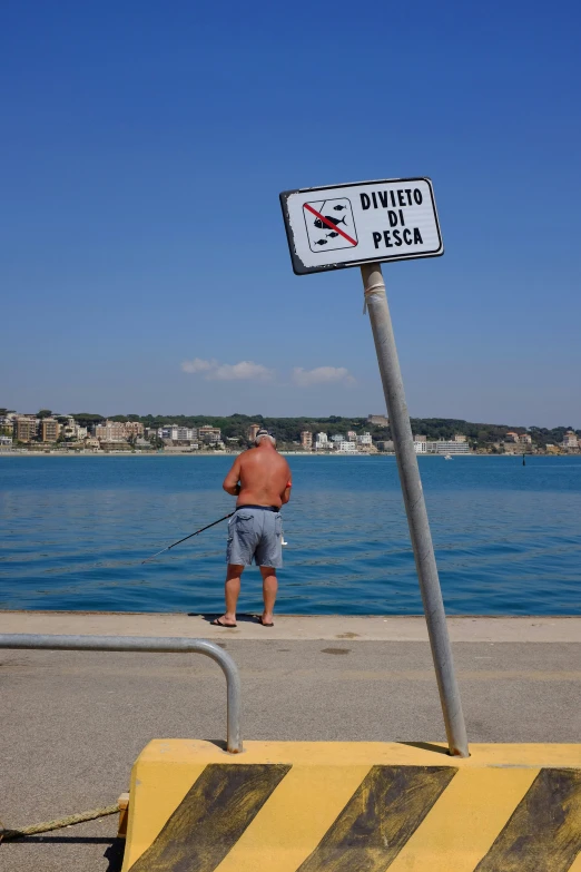 man fishing on a beach, under a no swimming sign