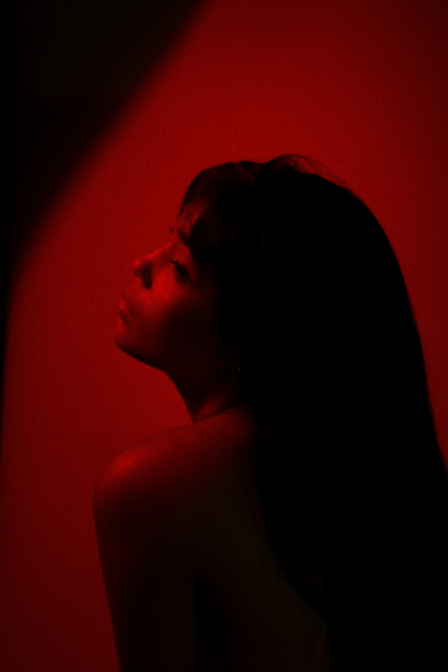 a woman with long hair looking down while standing in red light