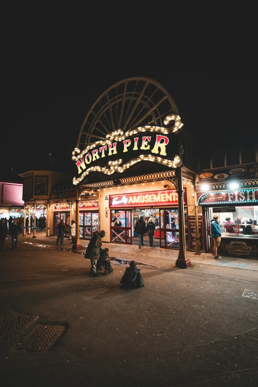 people are standing outside of a fairgrounds at night