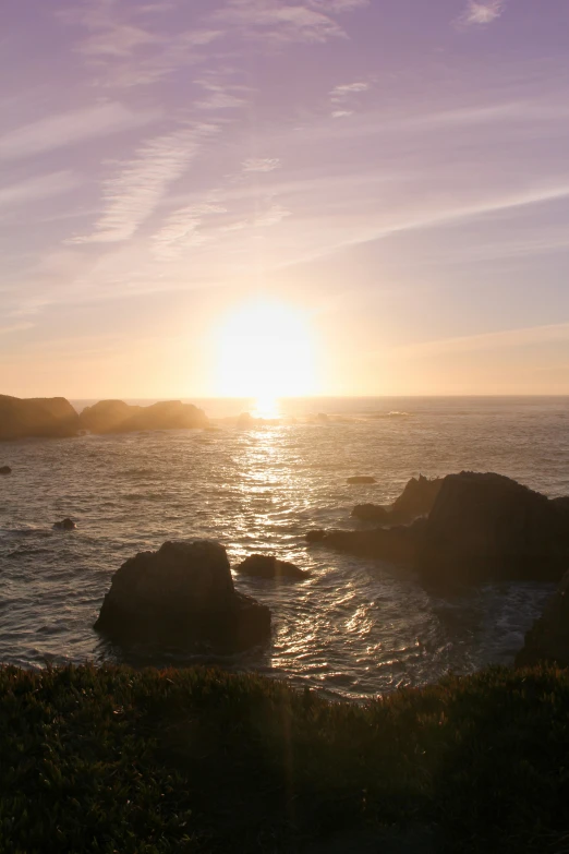 sun shining bright over an ocean and rocky coastline