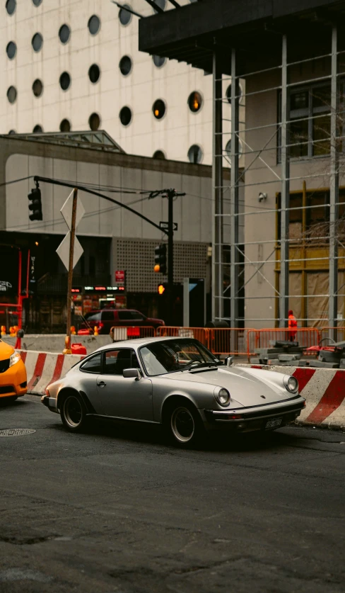 two porsches parked on the side of the road near some yellow traffic cones