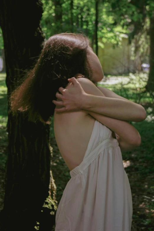 a woman wearing a white dress is leaning against a tree