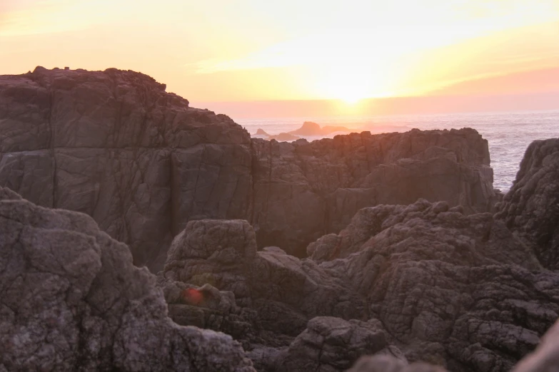 the sun is setting over some rocky shore