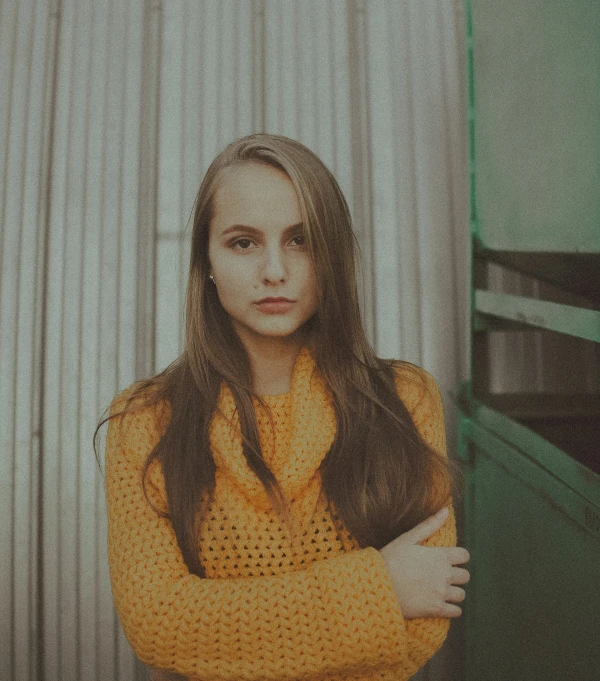 a young woman in a yellow shirt standing with her arms folded