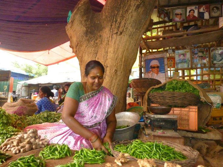 a woman sits with her hands in a bowl at a vegetable stand