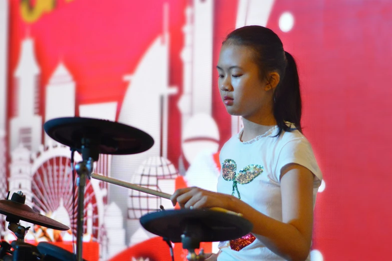  playing drums on stage with red backdrop