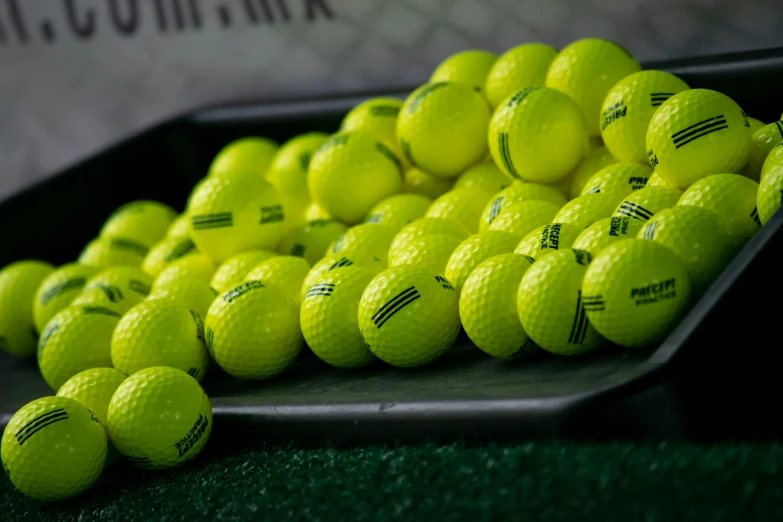 a tray of yellow golf balls on a green surface