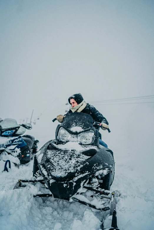 person riding snowmobile in snowy landscape next to other vehicles