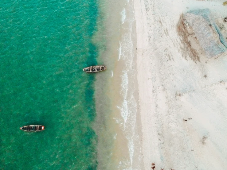 an aerial view of two boats in the sea near a beach