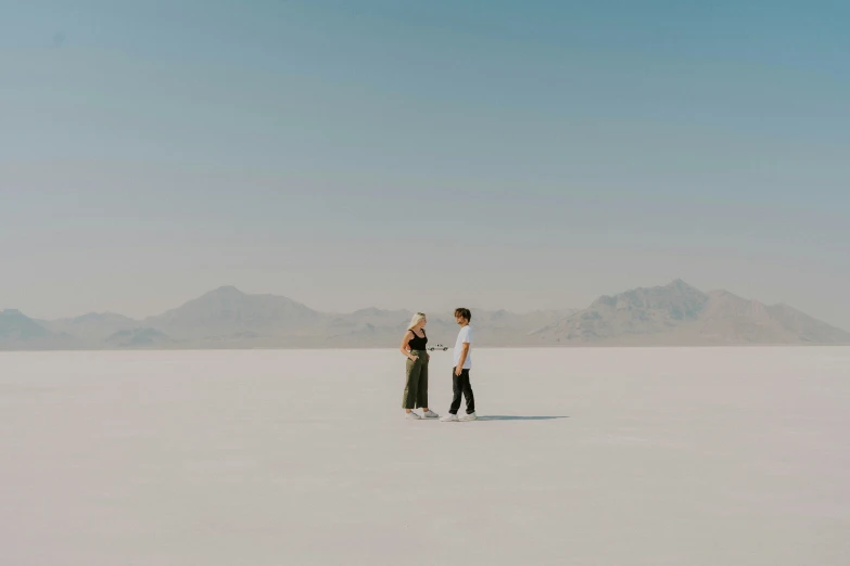 two people standing on a sandy plain with mountains in the background