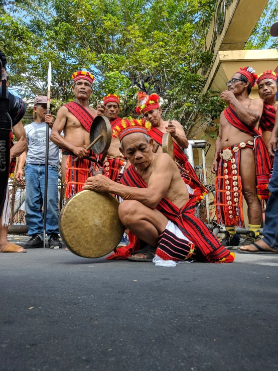 an indian man with a drum sits in front of a group of men with matching clothing and headgear