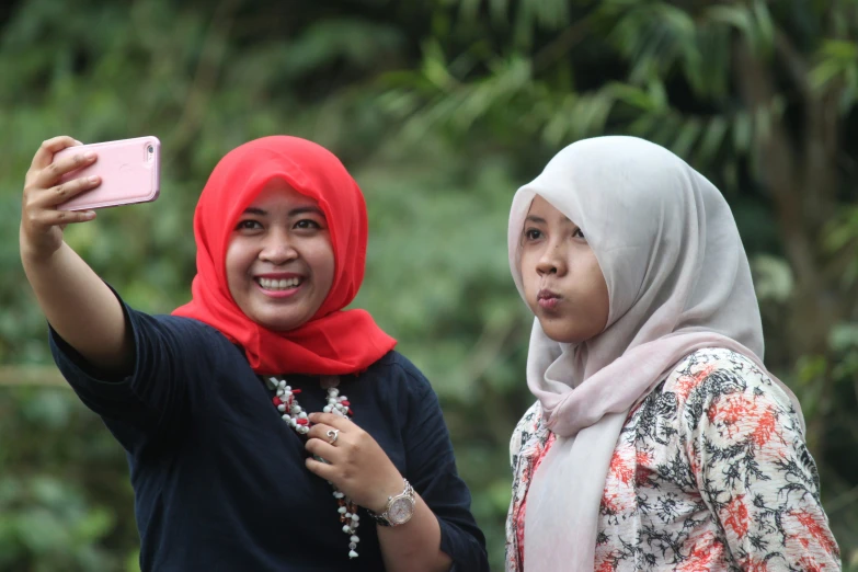 two women taking pictures while outside, one wearing a hijab