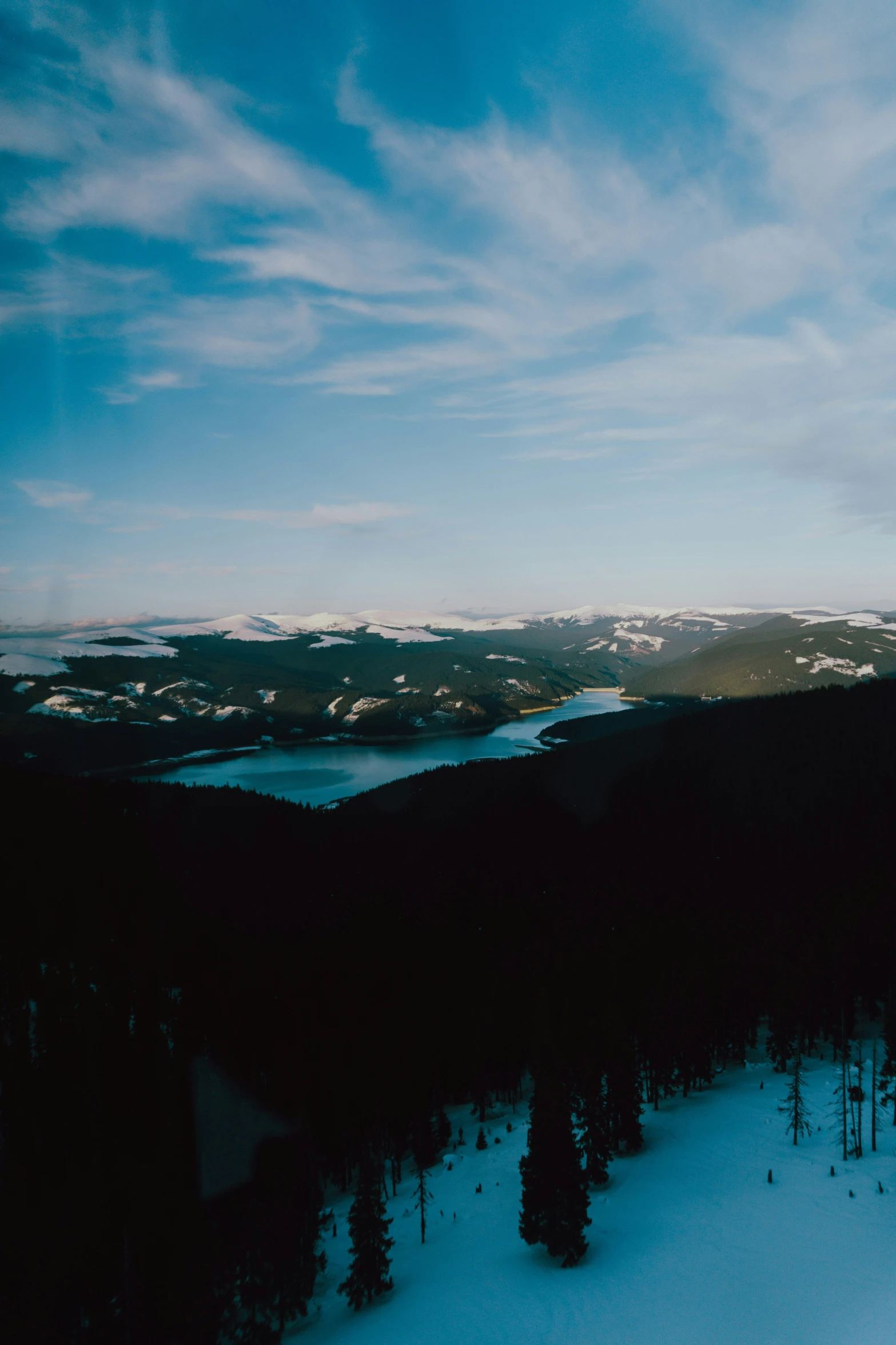 view of a snowy landscape of a forest, river, and mountains