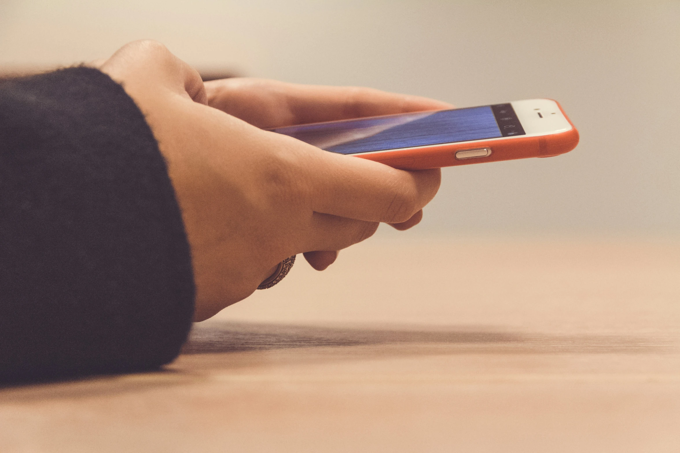 someone uses a phone while sitting on a wooden table