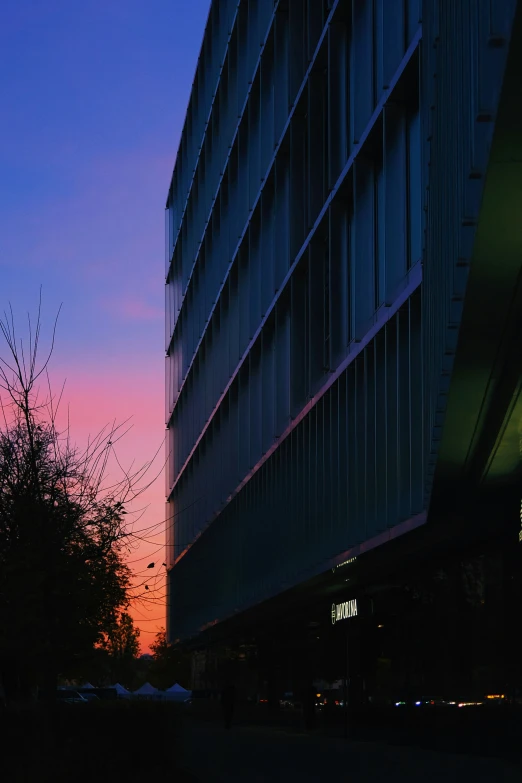 the sun sets behind a building next to a parking lot