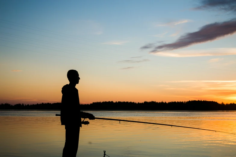 a man on a lake with a fishing pole at sunset