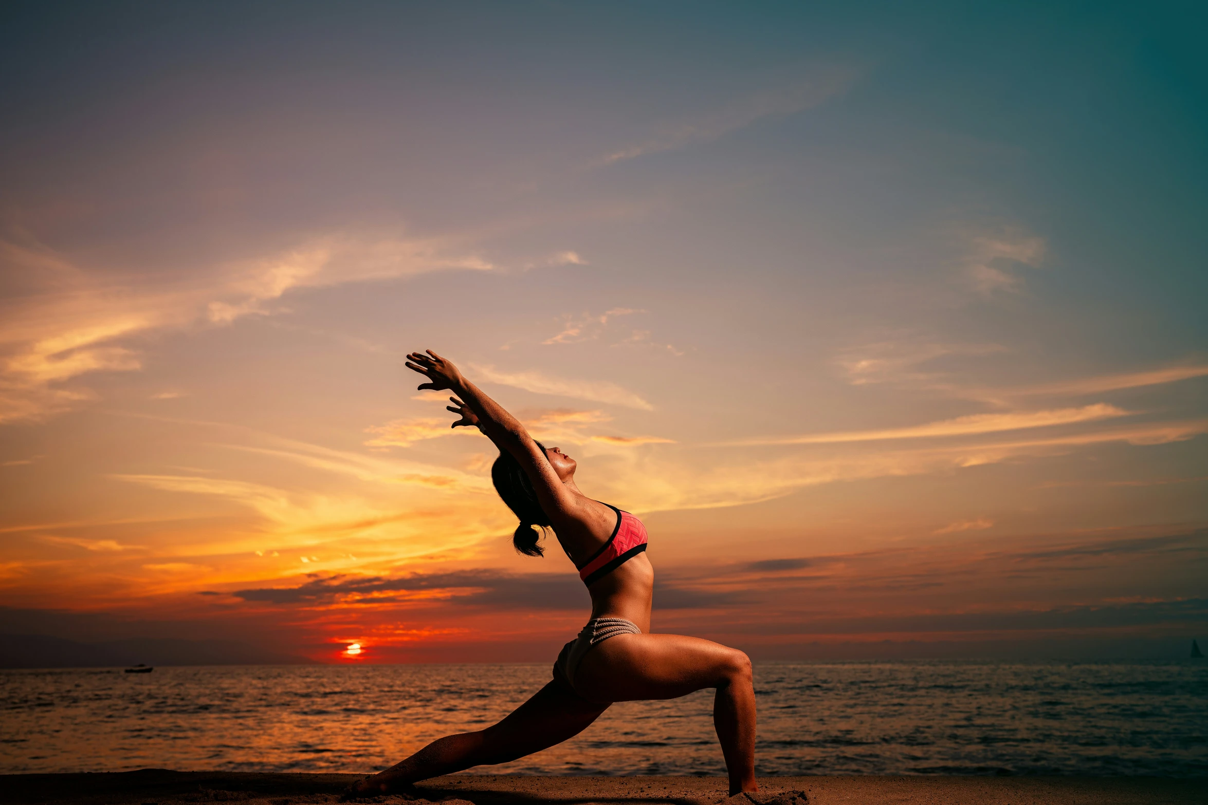 a woman practices yoga on the beach as the sun sets