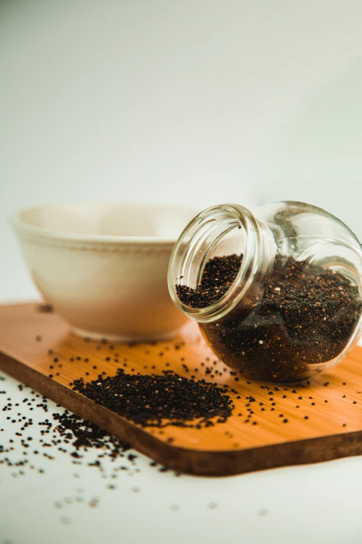 there is a glass jar full of black pepper sprinkles next to a white bowl
