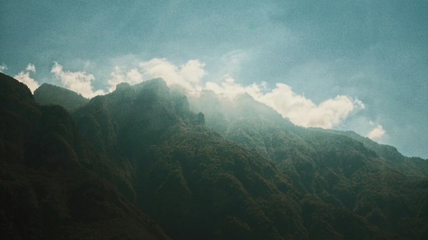 large mountains in the foreground with clouds and sun behind them