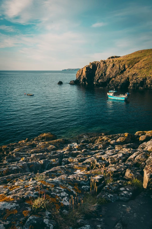 a boat is floating by a rocky cliff by the ocean