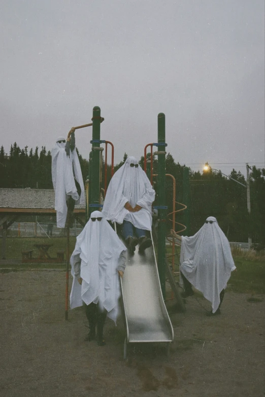several people wrapped in white cloaks are playing on the slide
