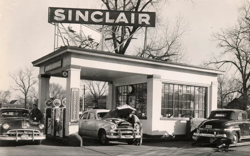 two old classic cars sitting at the gas station