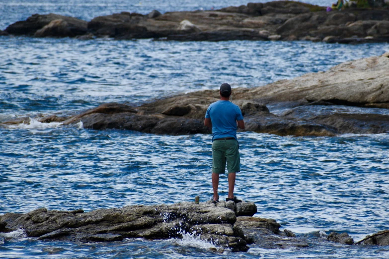 a man fishing off rocks on the ocean