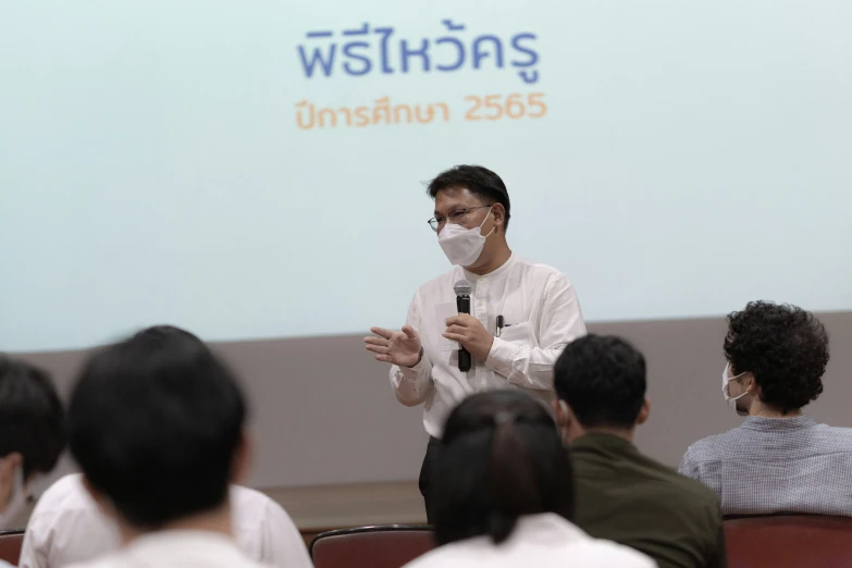 a man wearing a white mask speaks to a crowd