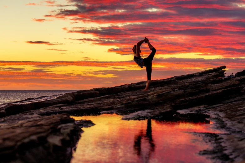 a person doing a handstand on top of a rocky cliff next to the ocean