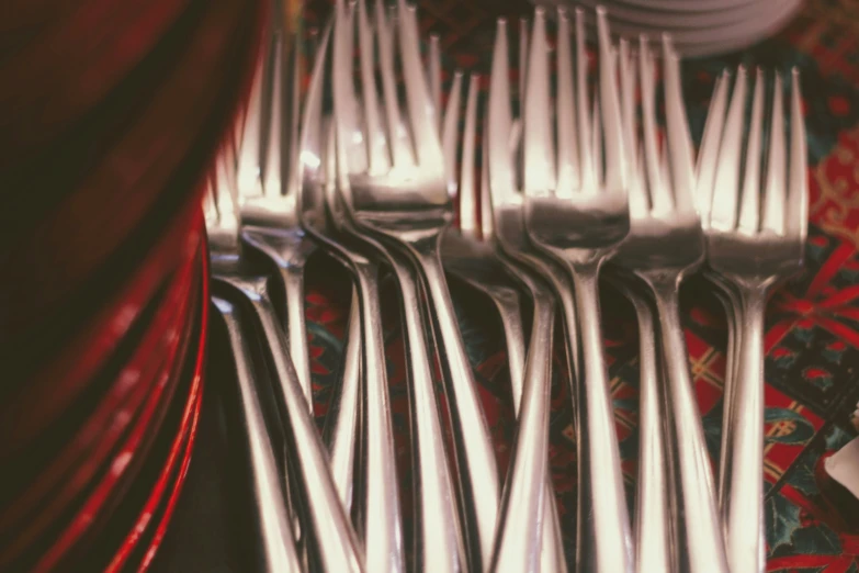 many silver forks are placed together on a red table