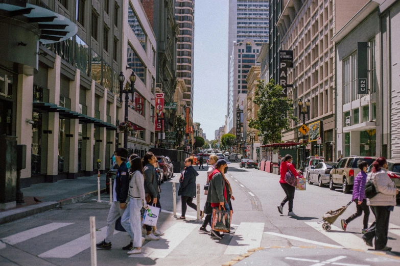 a group of people walking across a street next to tall buildings