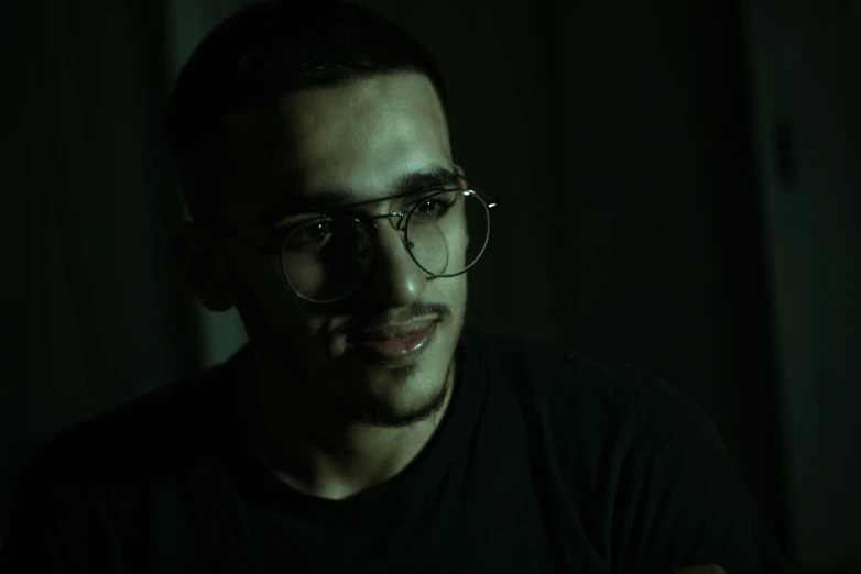 a man with glasses sitting down in a dark room