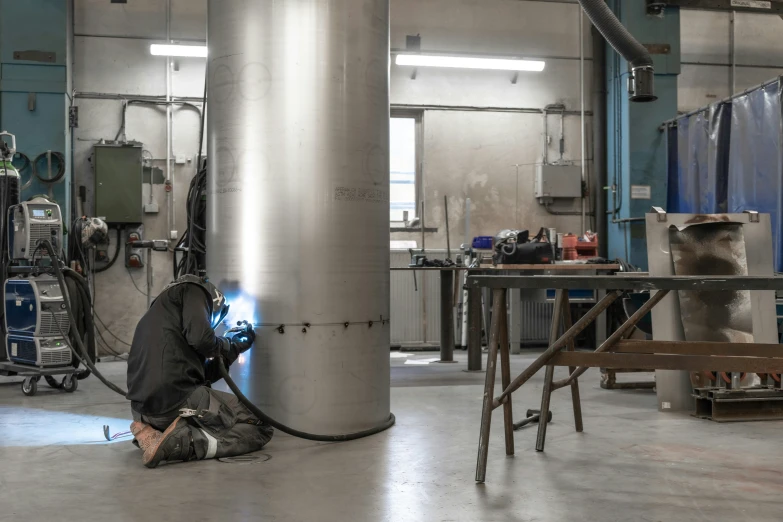 person welding a tank in a factory with blue walls